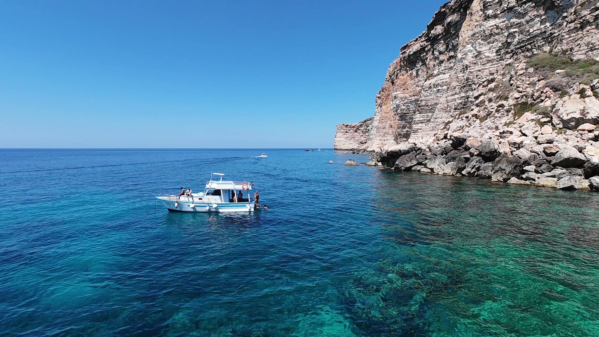 La Barca Gamar in sosta con ospiti in acqua vicino alla falesia